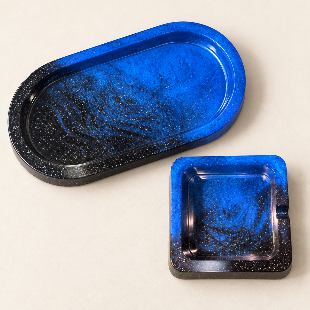 Matching blue and black glitter small oval tray and single-notch small square ashtray on cream background