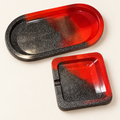 Matching red and black glitter small oval tray and single-notch small square ashtray on a clean cream background