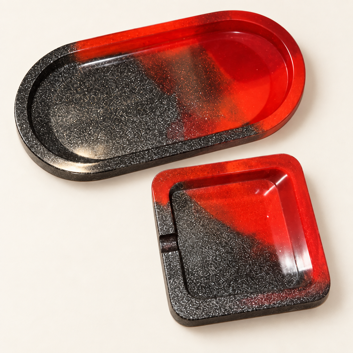 Matching red and black glitter small oval tray and single-notch small square ashtray on a clean cream background